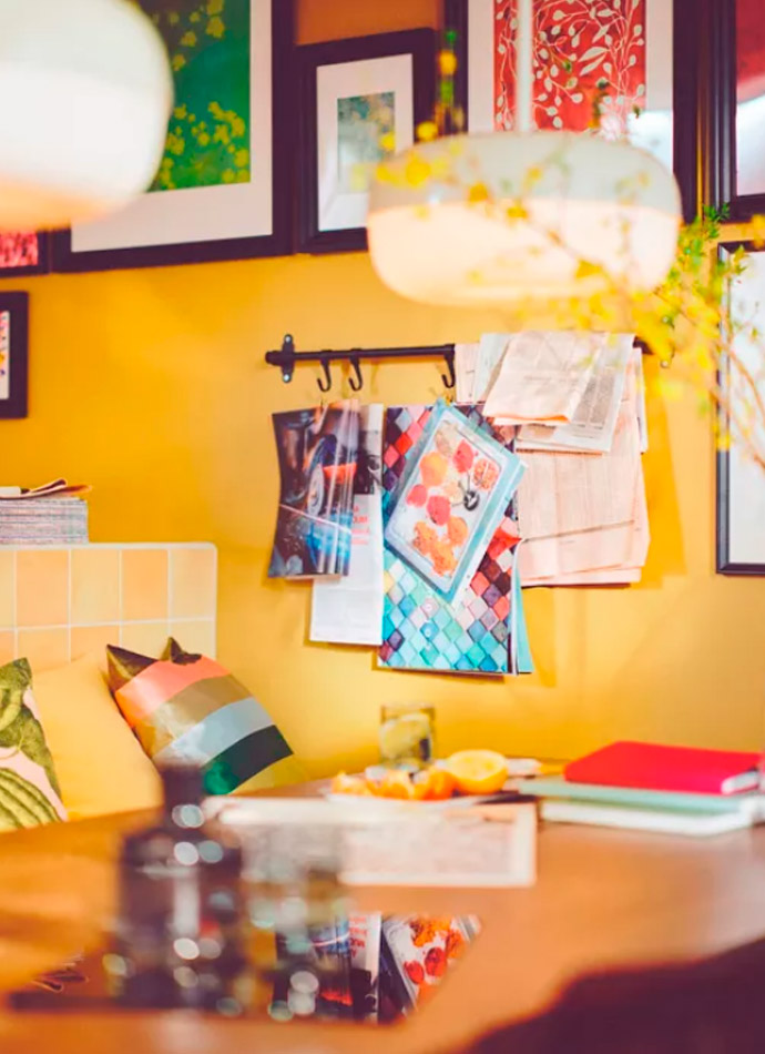 A wooden table with citrus and notebooks in front of a yellow wall with art and hooks. Warm atmosphere.