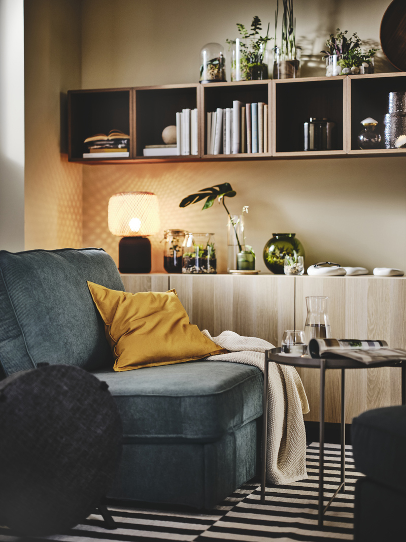 Ambiente de estilo moderno en madera de pino, hay un sillón gris y tiene un cojín mostaza y una manta encima, hay un mueble consola, y estantes de pared tipo caja.