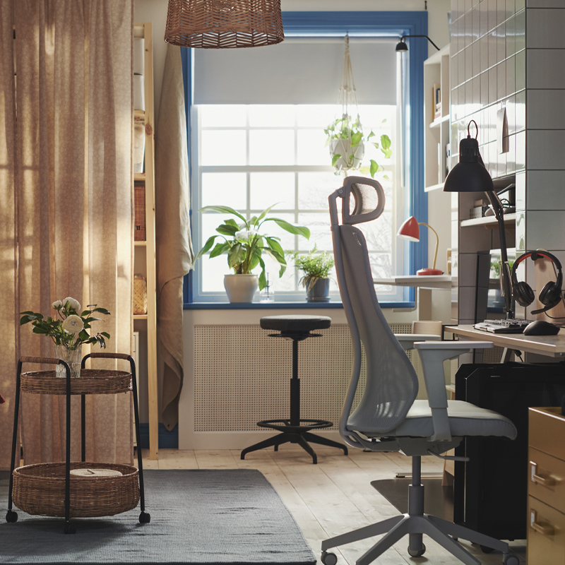 Multifunctional space with sofa, ergonomic chair workspace, blue-framed window, and sheer curtains. Warm ambiance.
