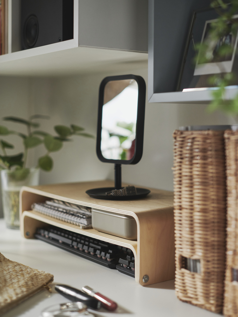 Organized desk with light wood stand, tabletop mirror, personal items, and wicker baskets.