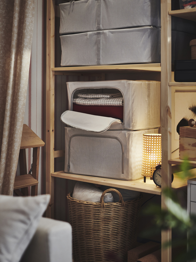 Wooden shelving unit with grey organizing boxes, a wicker basket, and an ambient lamp with warm light.