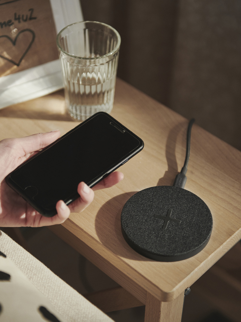 Hand holding a black phone near a round wireless charger, on a wooden table.