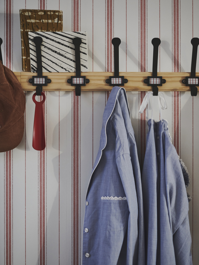 Wooden coat rack with black hooks, blue jackets, and red shoehorn, on a red and white striped wall.