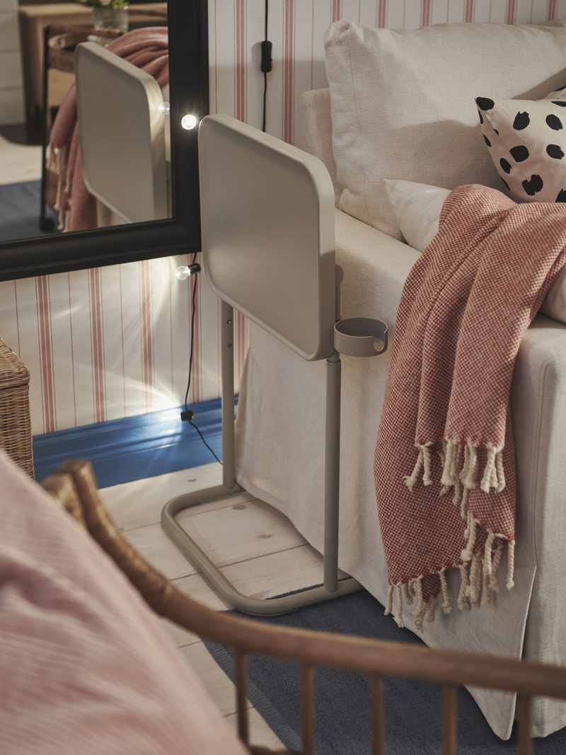 Bed with pink blanket, gray adjustable side table next to mirror with lights, on wood floor and blue rug.