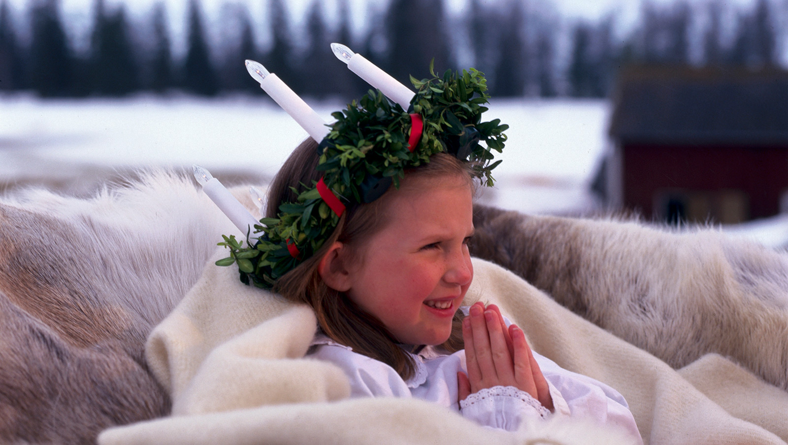 Una niña con un vestido blanco y una corona con velas blancas celebrando Santa Lucía.