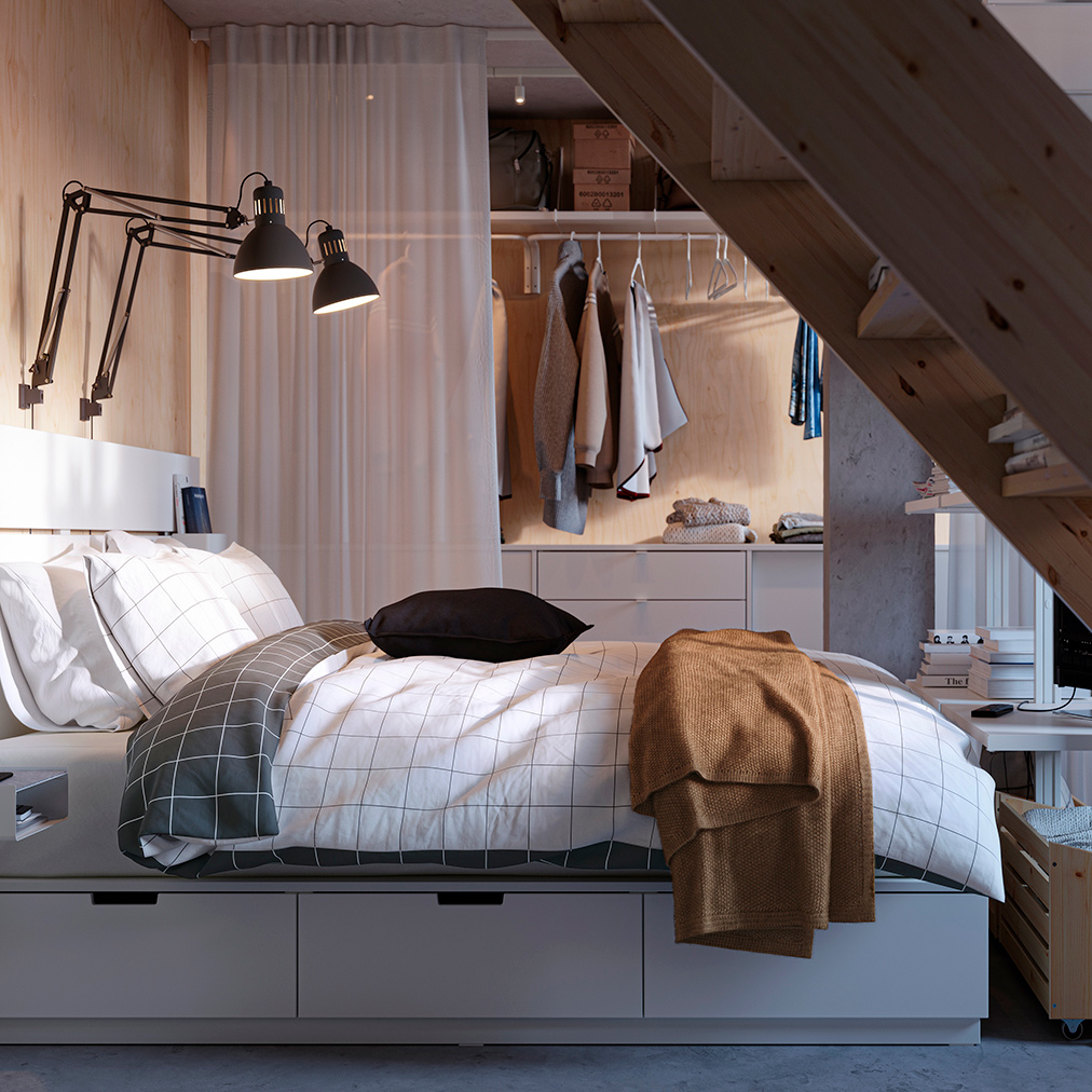 Dormitorio compacto con cama blanca, almacenamiento integrado y escalera de madera expuesta.