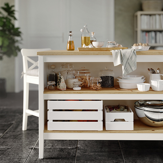 Detalle de la parte inferior de una isla de cocina con base blanca y encimera de pino con cajas de madera y vajilla en la parte inferior.