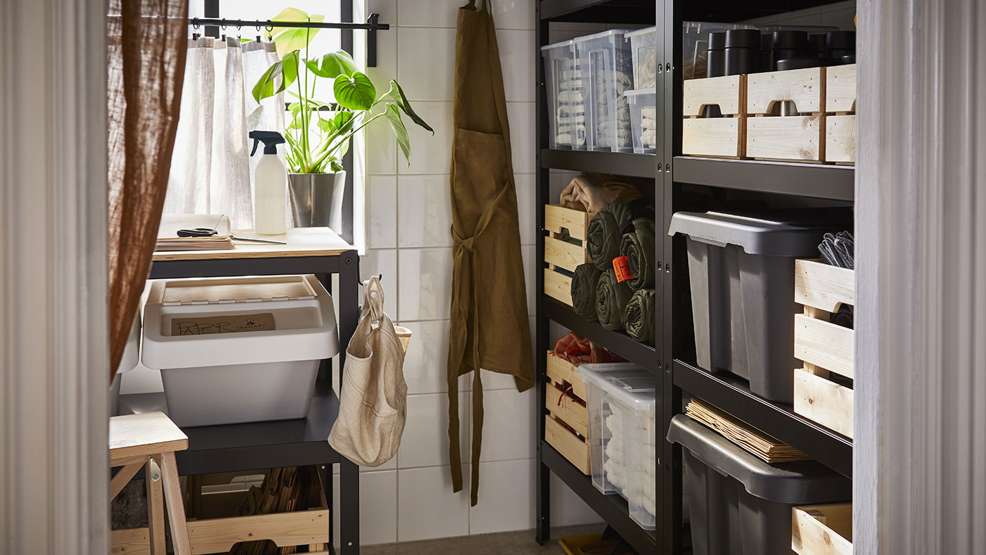 Un cuarto de almacenaje con un banco de trabajo BROR, un tacho de reciclaje SORTERA y, a la derecha, una estantería BROR con cajas KNAGGLIG y SAMLA.