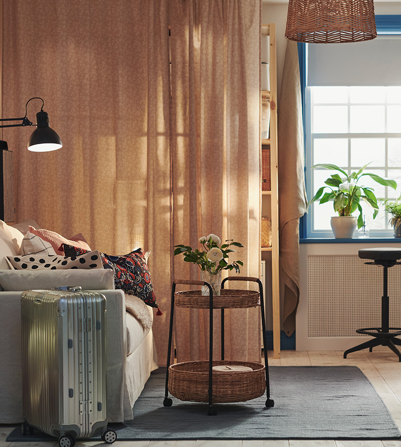 Cozy room with a study area, sofa, plants, and natural light coming through a large window.