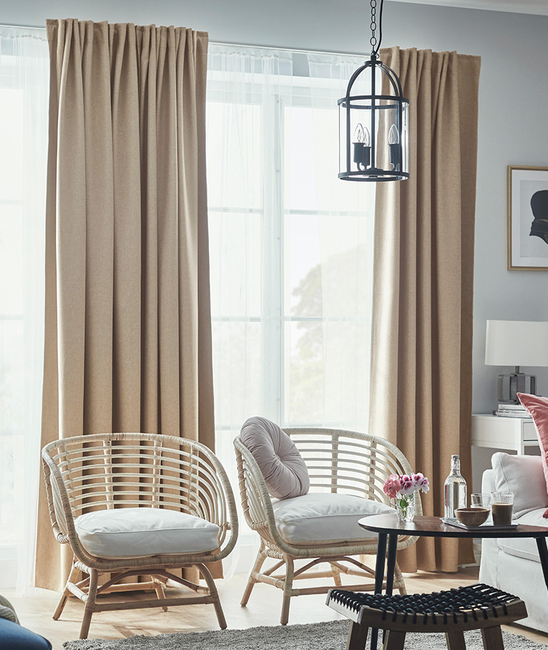 Bright living room with beige curtains, rattan chairs, and a cozy coffee table set near a large window.