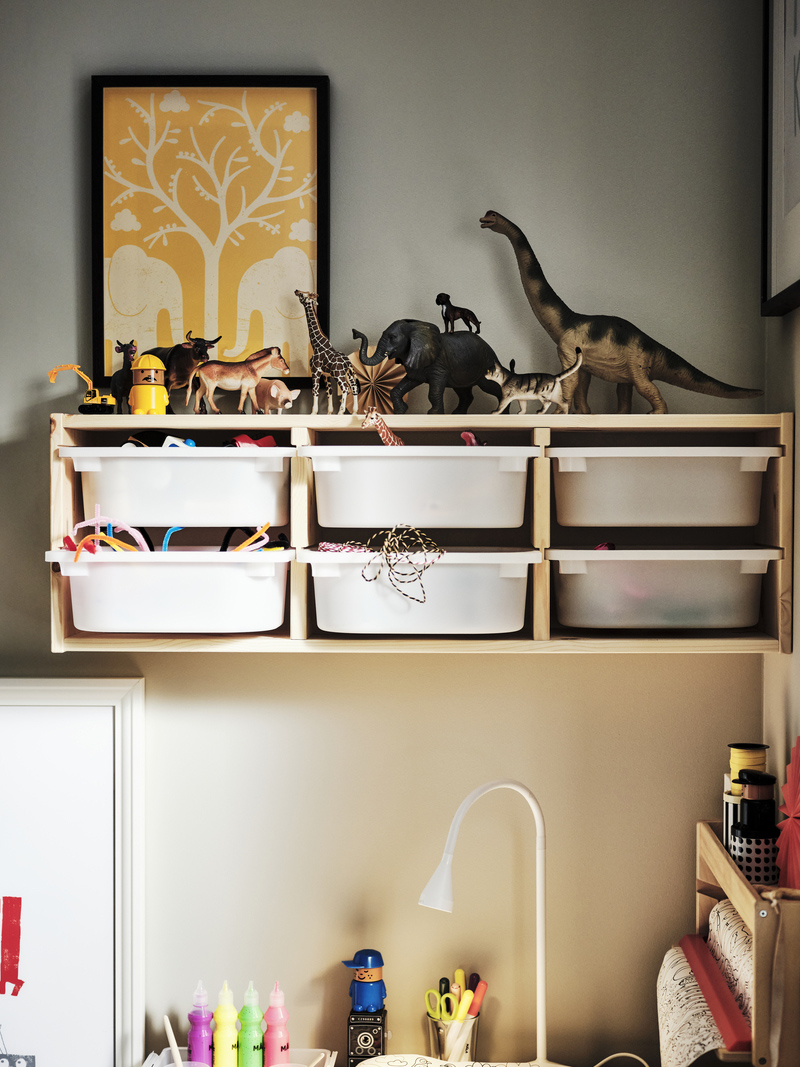Children's bedroom with wooden shelves and white organizing boxes filled with toys. A yellow tree poster decorates the wall, creating a playful ambiance.