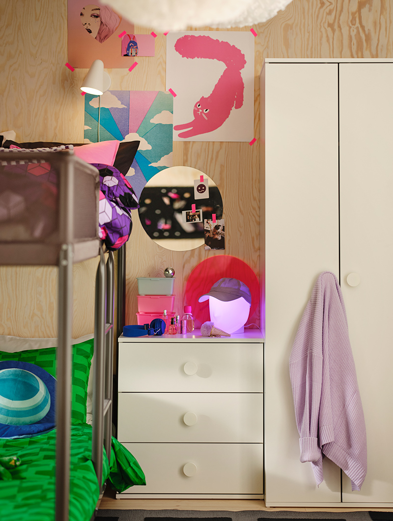 Dormitorio juvenil con literas, cómoda blanca y armario. Pósters vibrantes y luces rosadas crean un ambiente alegre y personalizado.