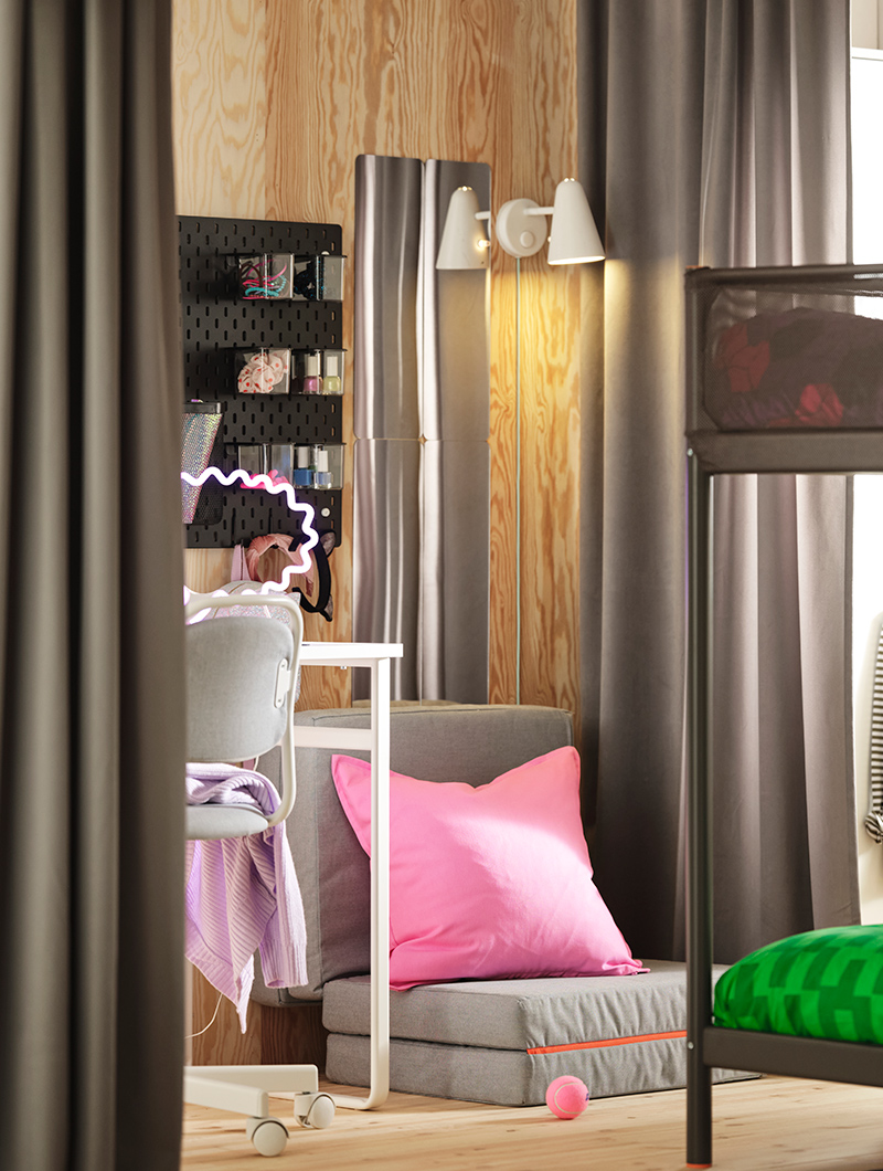 Dormitorio juvenil con literas, escritorio y cortinas grises. Un cojín rosa vibrante y una luz de neón añaden un toque moderno y divertido.