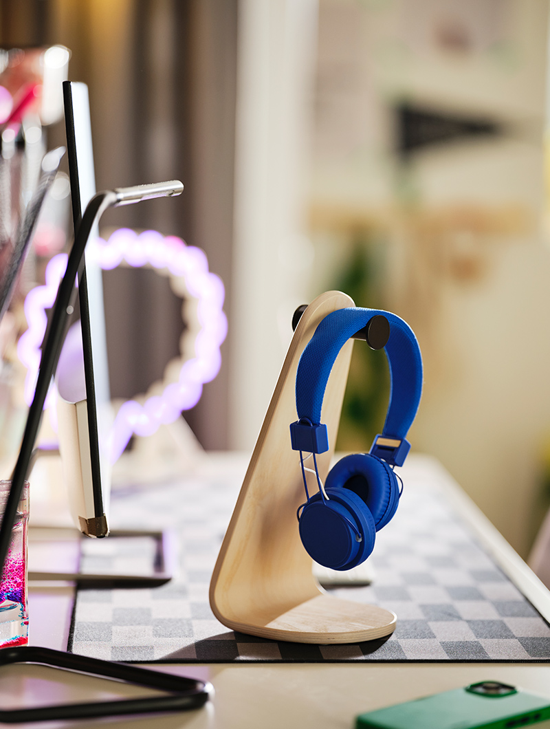 Auriculares azules en un soporte de madera sobre un escritorio con alfombrilla de ajedrez. Un ambiente de estudio juvenil y organizado.
