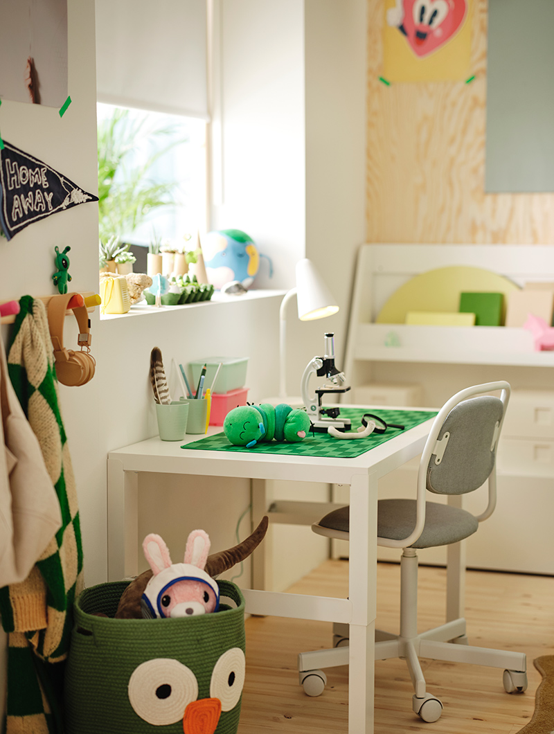 Dormitorio infantil con un escritorio blanco, silla gris y un microscopio sobre una alfombrilla verde. Ambiente luminoso y propicio para el estudio y juego.