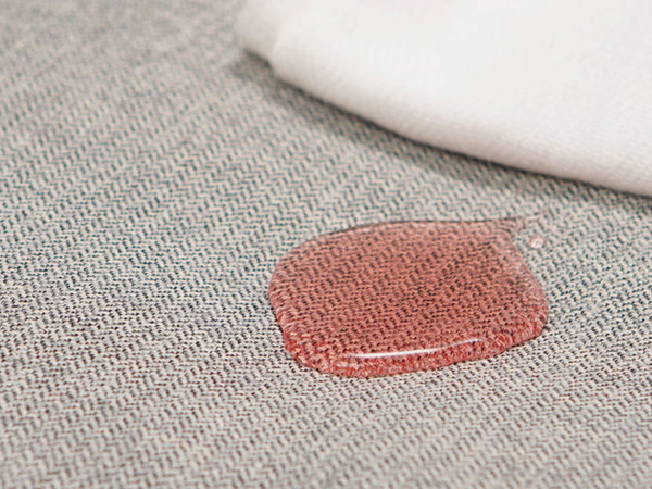 Textil claro con derrame rojo y paño para limpieza fácil