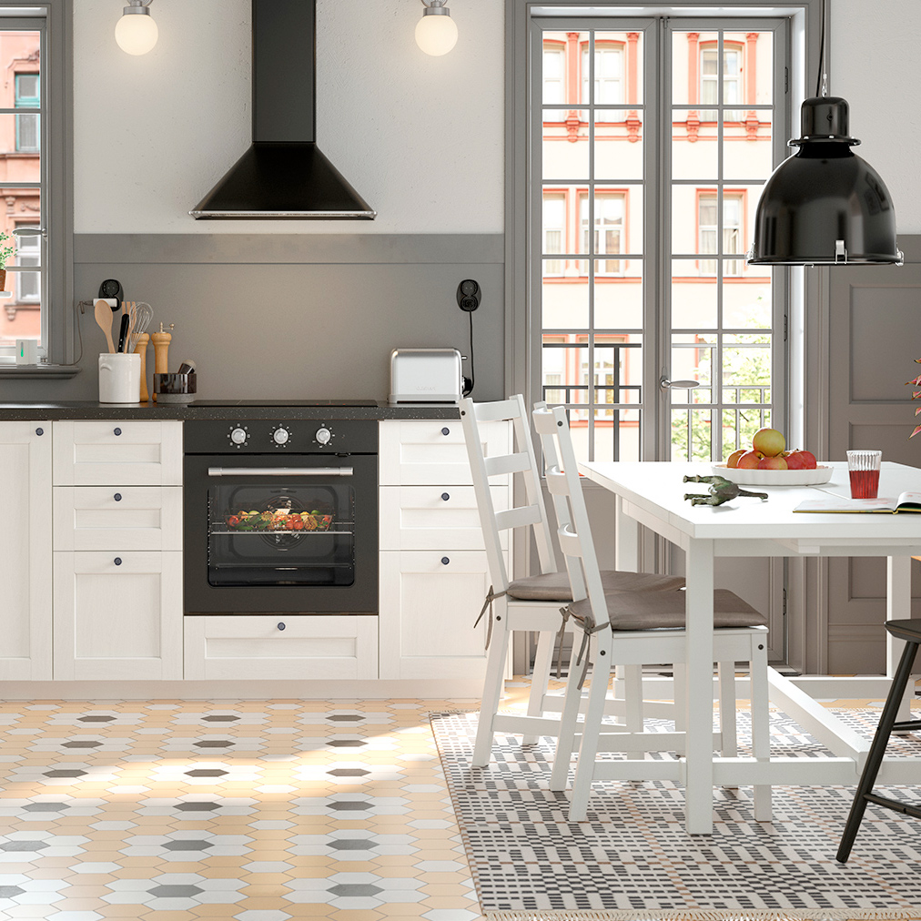 Cocina moderna y luminosa con gabinetes blancos, detalles en negro y un acogedor comedor. El suelo combina patrones para dar dinamismo al ambiente.