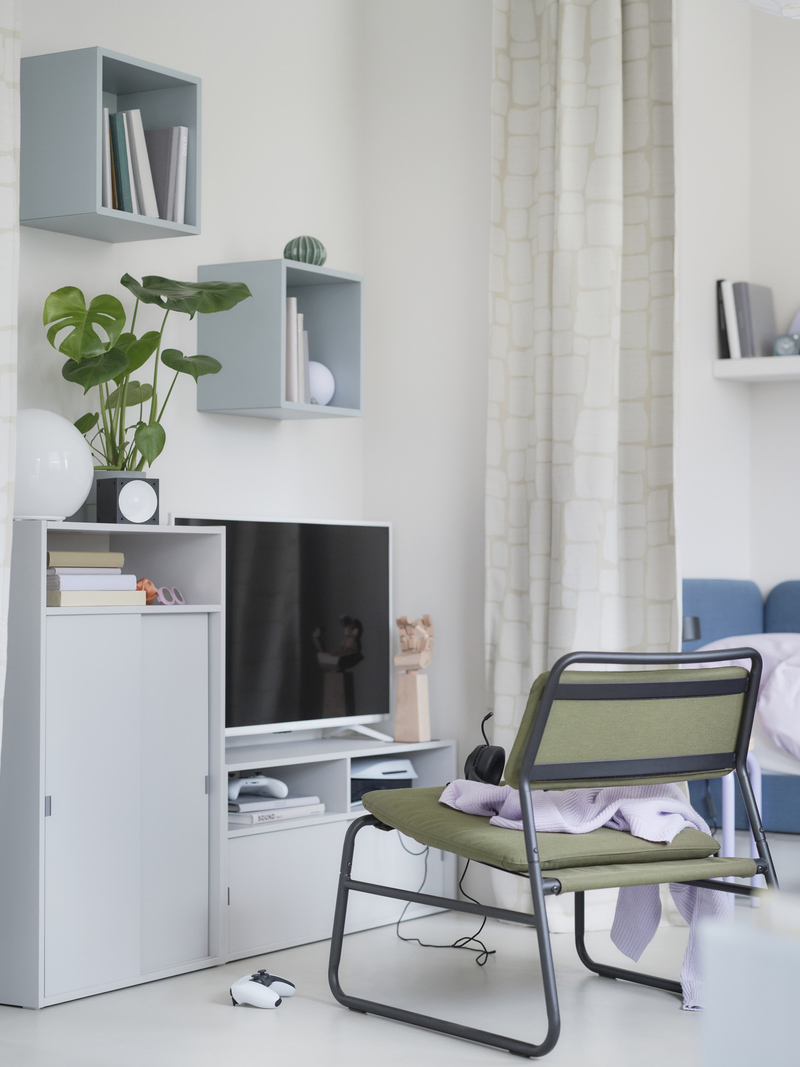 A green armchair with a SPIKSMED cabinet, EKET shelving unit, and LÖNNSTÄVMAL blackout curtains.