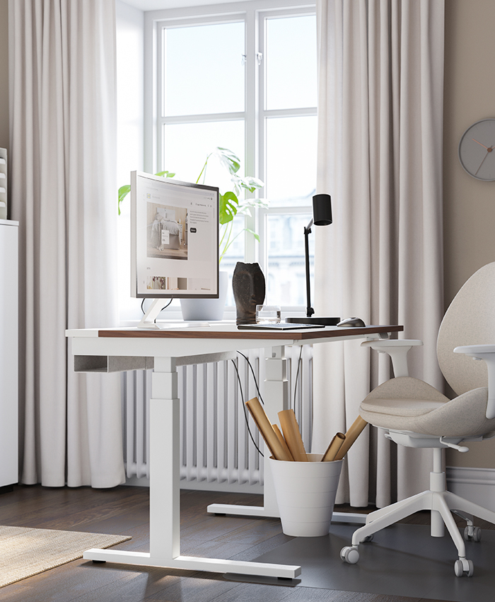 Espacio de trabajo con escritorio blanco ajustable, silla ergonómica beige, monitor y luz natural desde la ventana.