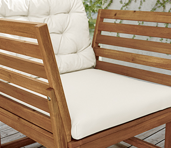 Sillón de jardín de madera con cojines blancos, respaldo de listones y estructura robusta sobre suelo de madera.