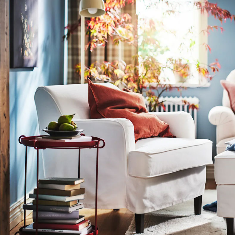 Rincón de lectura de estilo tradicional con un cómodo sillón, cojines y mantas, velas y flores para crear un ambiente relajante.