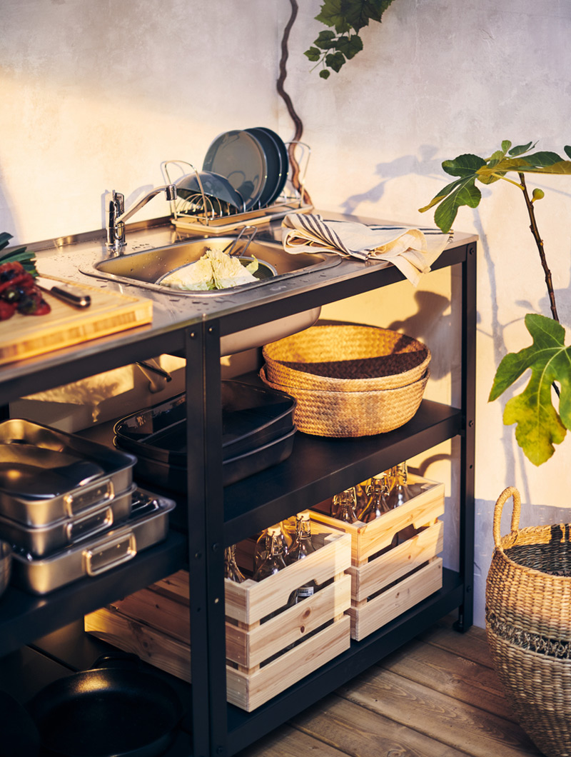 Outdoor sink station with dark shelves and wooden crates. Clean dishes and utensils create a practical and tidy ambiance.