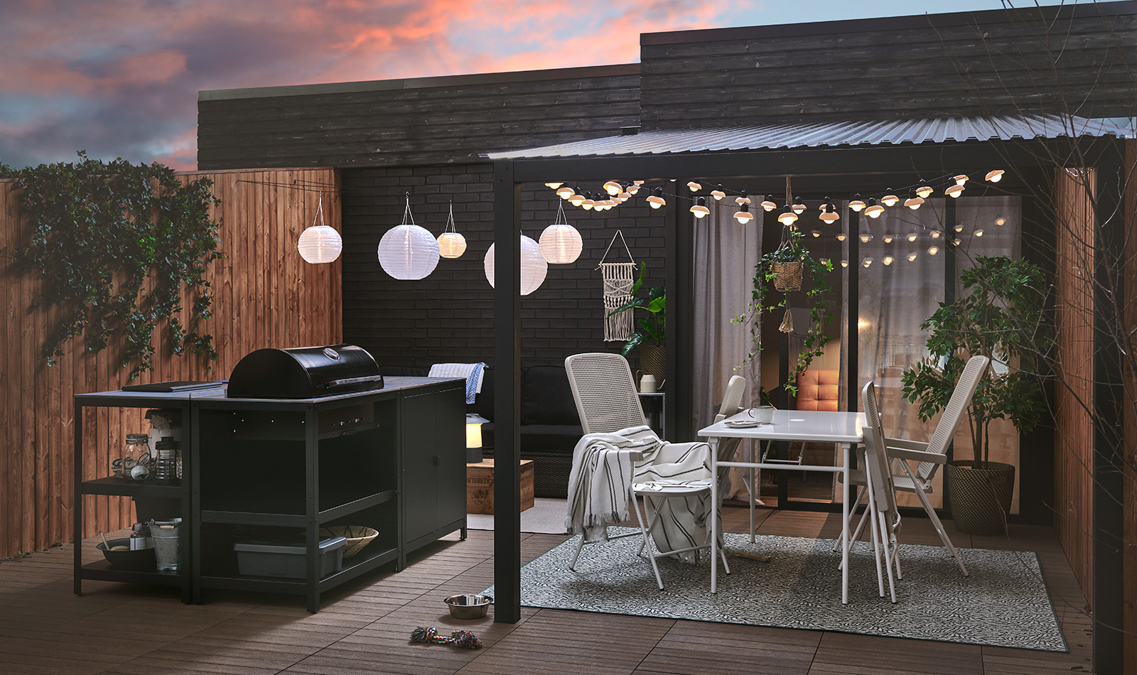 Dark patio with grill, outdoor dining set, and white string lights. Creates a cozy nighttime ambiance for outdoor gatherings.