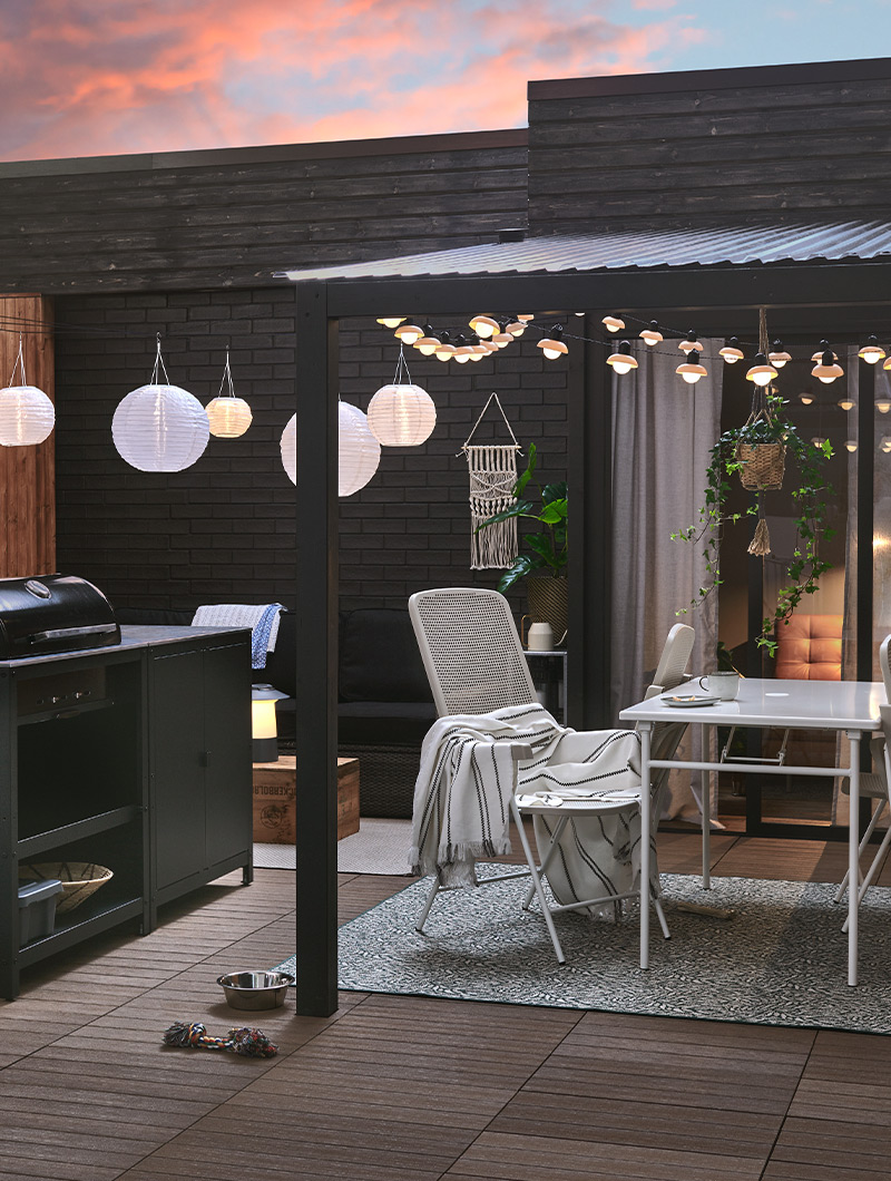 Dark patio with grill, outdoor dining set, and white string lights. Creates a cozy nighttime ambiance for outdoor gatherings.