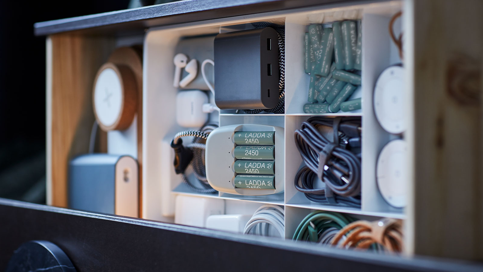 Cajón organizado con baterías, cables, cargadores y accesorios tecnológicos en compartimentos.