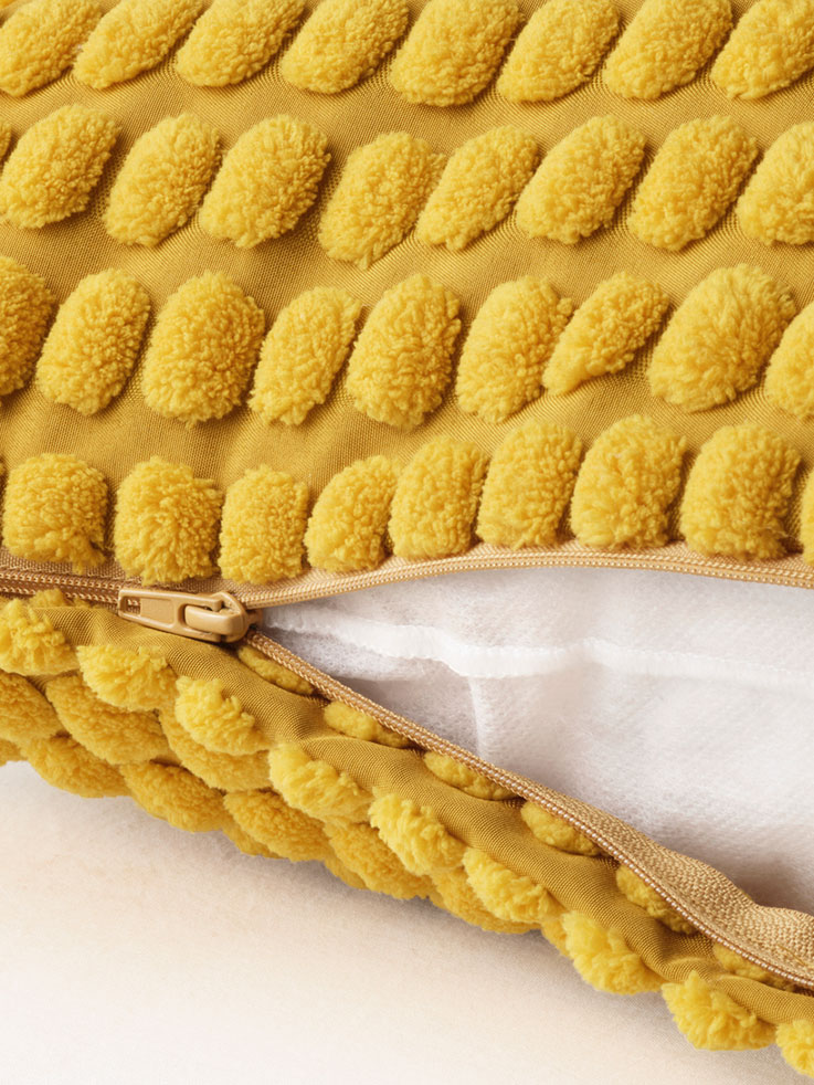 Primer plano del cierre de un cojín amarillo, se puede ver la textura esponjosa de la funda.