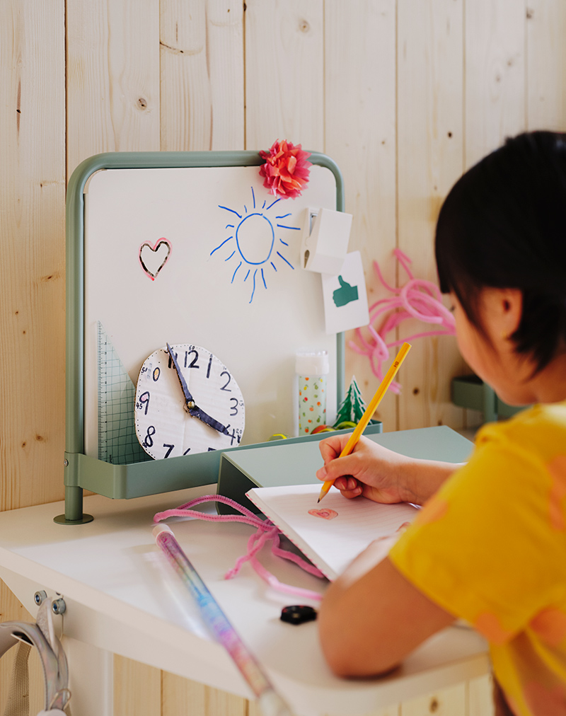 Una niña escribiendo sobre una tabla de escritura RELATERA colocada en una combinación de escritorio RELATERA.