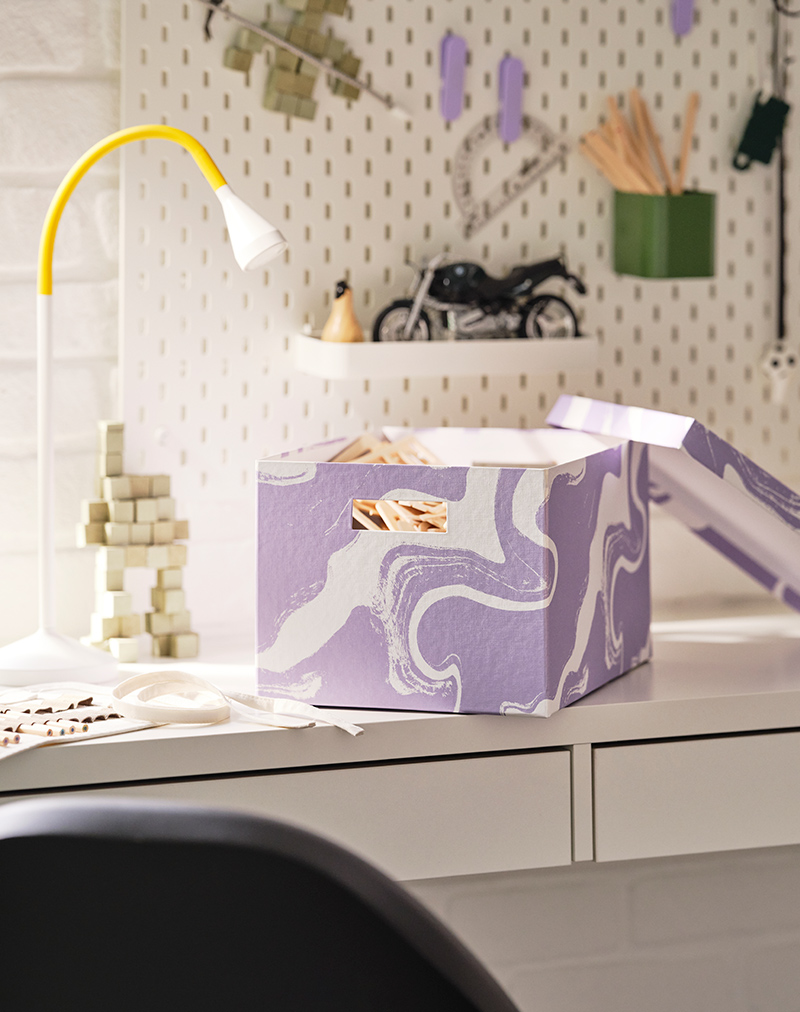 Una caja de almacenamiento sobre un escritorio MICKE con un tablero SKÅDIS blanco al fondo
