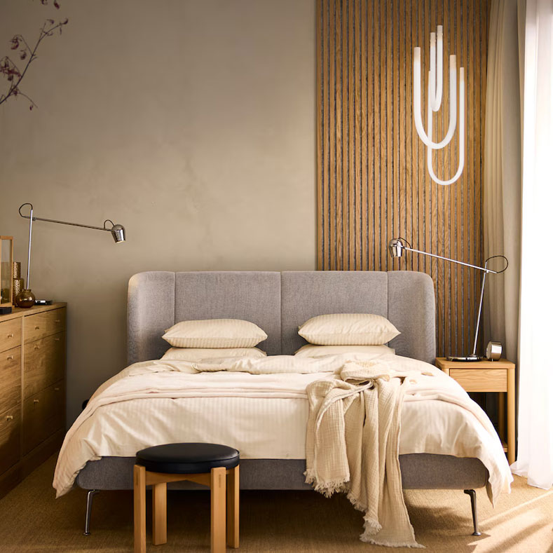 Modern bedroom with gray bed, wooden dresser, clothes rack, and warm accents. Cozy atmosphere.