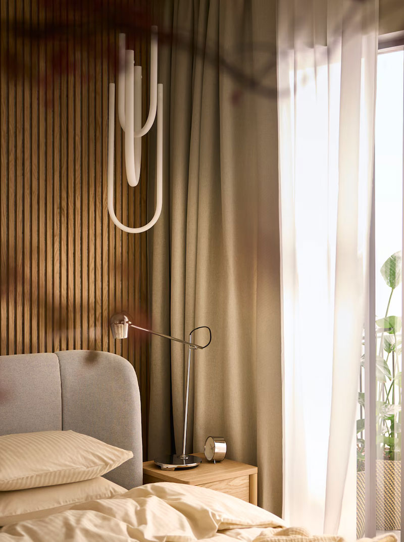 Designer lamp on wooden nightstand, gray headboard, beige curtains. Bright and modern atmosphere.