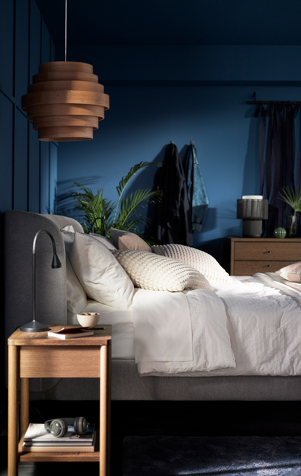 Cozy bedroom with soft lighting, wooden nightstand, and neutral bedding in a dark blue setting.