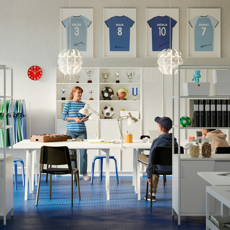 Sala de estudio y creatividad para niños, hay estanterías modernas con libros, hay pupitres con ordenadores y al fondo estanterías con trofeos deportivos y balones y camisetas de fútbol enmarcados.