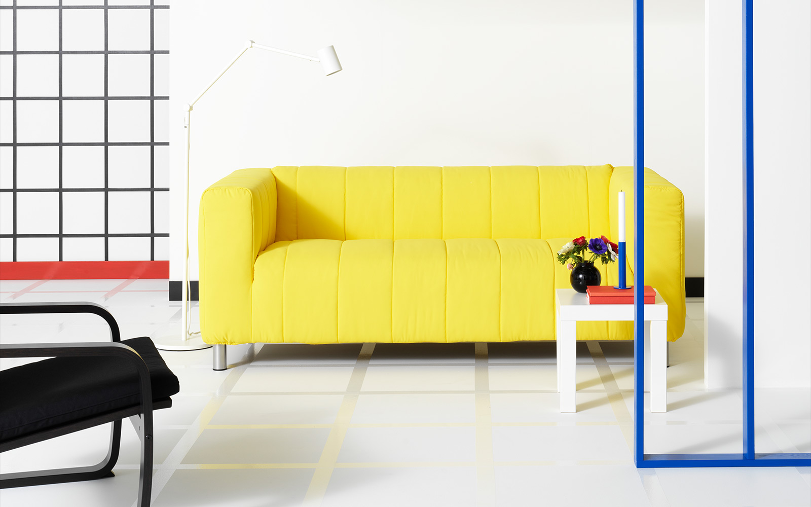 Sofá KLIPPAN de 2 asientos color amarillo con una mesa auxiliar LACK y una lámpara de piso NYMANE, todo ubicado en una sala.