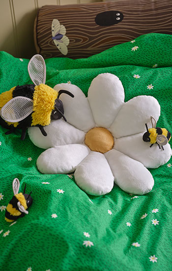 Kids' bed with green daisy sheets, plush bees, and a large flower. Playful and natural atmosphere.