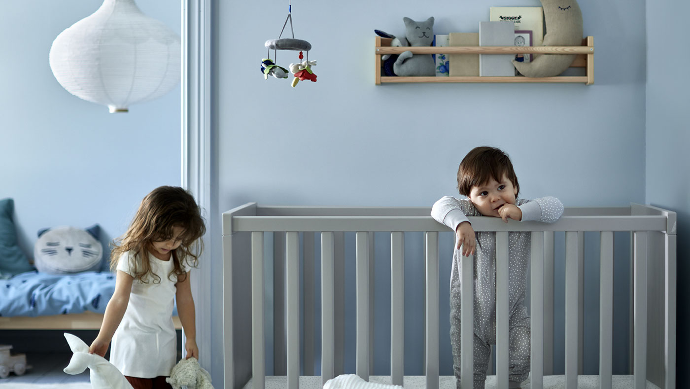 Un bebé en una cuna SUNDVIK, un almacenamiento de pared FLISAT y una lámpara colgante RISBYN.