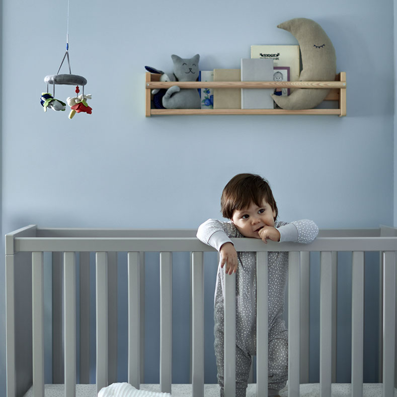 Un bebé en una cuna SUNDVIK, un almacenamiento de pared FLISAT y una lámpara colgante RISBYN.