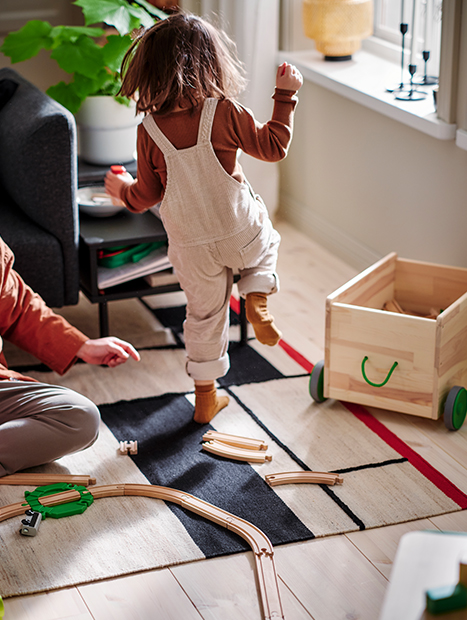 Woman and girl playing together with wooden rails on a modern rug. 