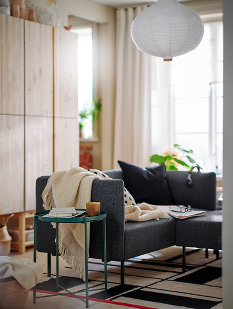 Living room with a sofa with a throw, a table and a chair, decorated in a modern way.