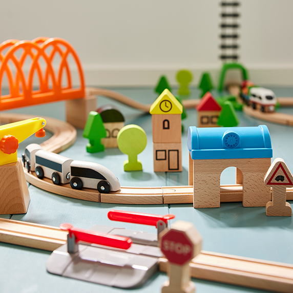 Pista de tren de madera con edificios de colores, puente naranja. Ambiente de juego infantil creativo.