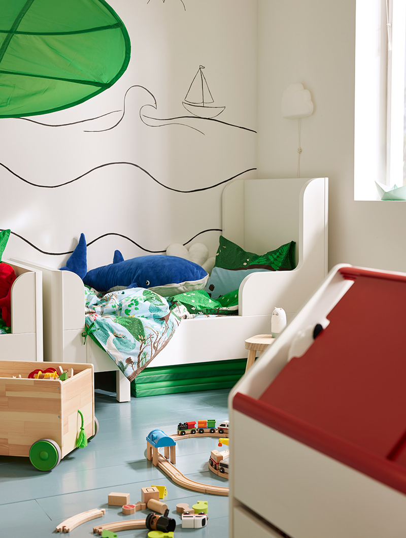 Habitación infantil blanca con cama, almohada de ballena azul y tren de madera. Ambiente lúdico.