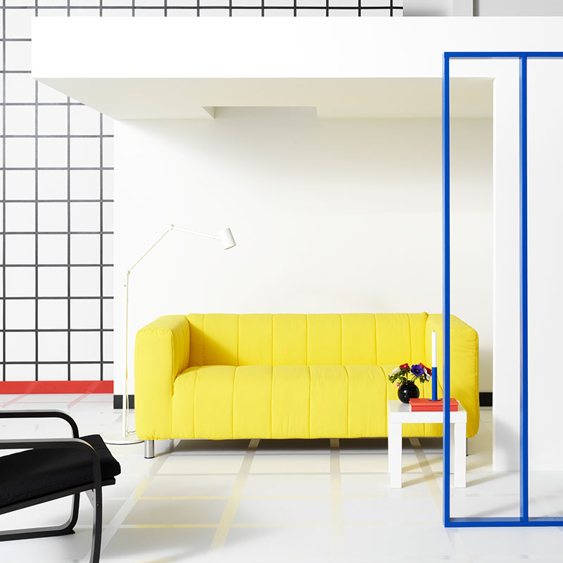 Sofá KLIPPAN de 2 asientos color amarillo con una mesa auxiliar LACK y una lámpara de piso NYMANE, todo ubicado en una sala.