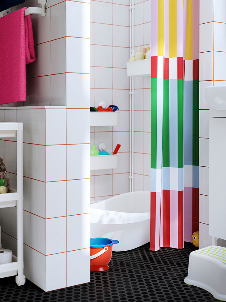 White kids' bathroom with multicolor shower curtain, pink towels, and colorful toys.