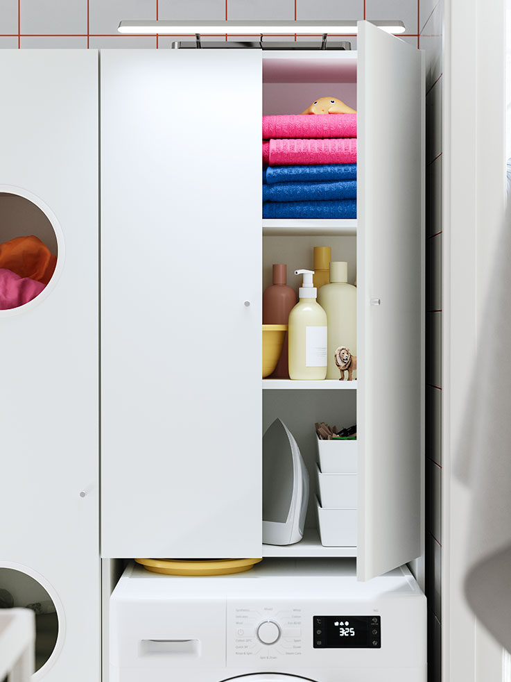  Open white cabinet with pink/blue towels, products, and iron over washing machine. Functional ambiance.