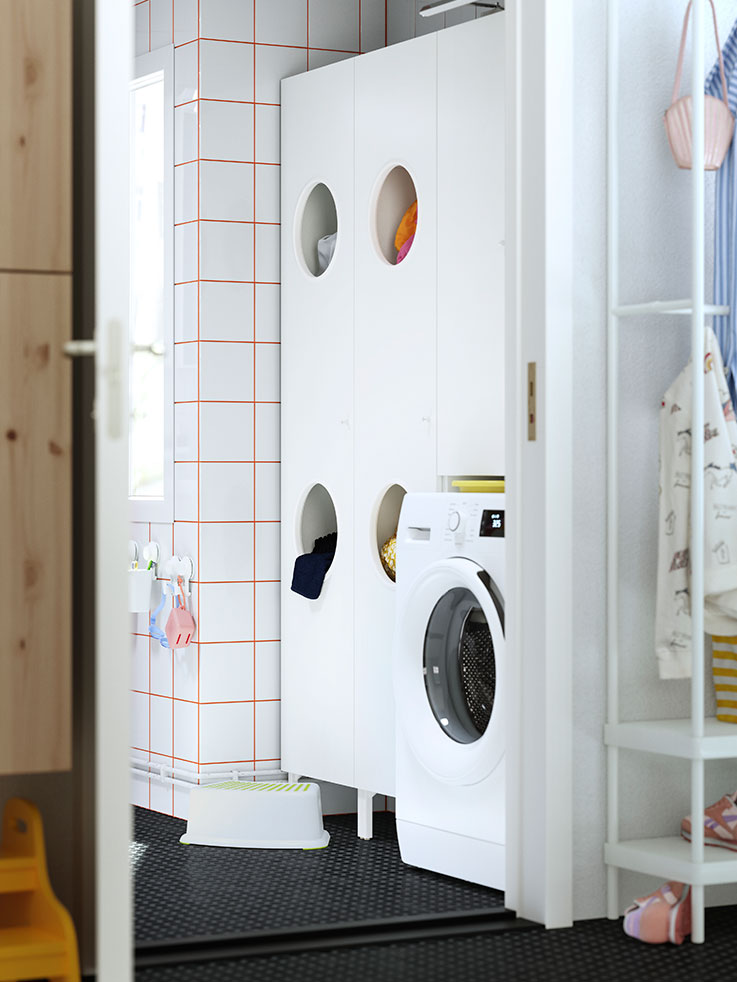  White bathroom with orange tiled grout. Washing machine and storage cabinets. Functional ambiance.