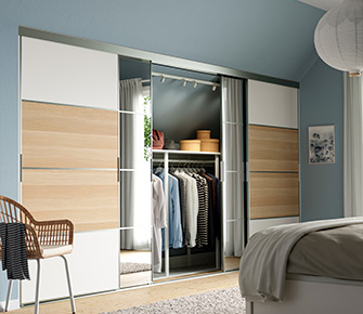 PAX wardrobe with sliding doors, one mirrored, interior with hanging clothes and storage boxes; bedroom decorated in soft tones.