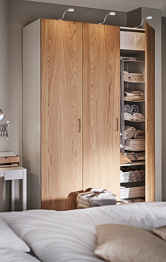 Partially open wooden wardrobe with shelves filled with towels and storage boxes, lit by overhead spotlights.